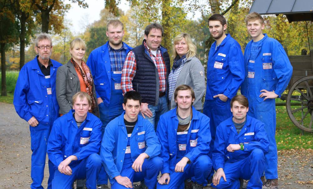 Gruppenfoto von Mitarbeitern in blauen Overalls, draußen in der Natur.