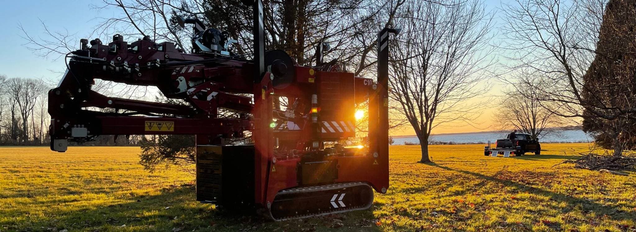 Hoeflon Kran in der Sonne, mit einem Lkw im Hintergrund und Bäumen drumherum.